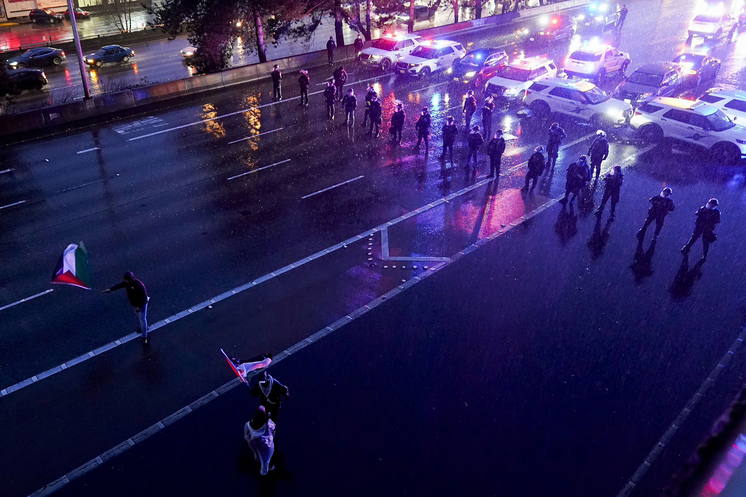 caption: Protesters calling for a cease-fire in the Israel-Hamas war wave Palestinian flags in front of a Washington State Patrol blockade as they leave after blocking Interstate 5 northbound for several hours Saturday, Jan. 6, 2024, in downtown Seattle. 