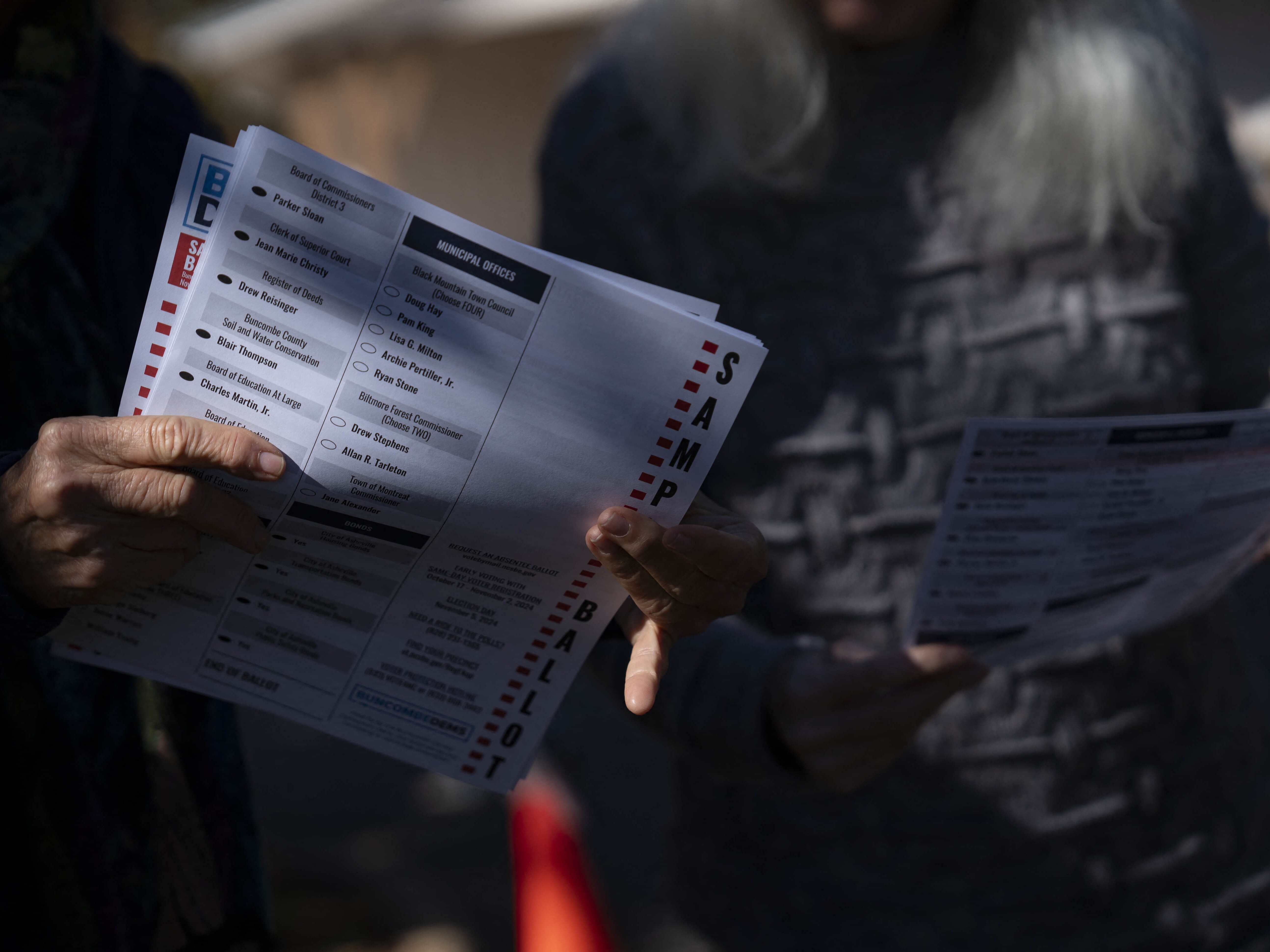 caption: A woman holds a sample ballot on the second day of early voting at a polling station, October 18, 2024, in Fairview, North Carolina. Despite concerns about early voting access after Hurricane Helene, many local officials reported record turnout for early voting, like in nearby Yancey County.