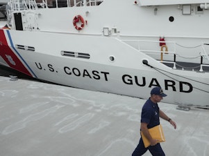 caption: U.S. Coast Guard Cutter Warren Deyampert is docked Tuesday as a member of the Coast Guard walks past at Coast Guard Base Boston.