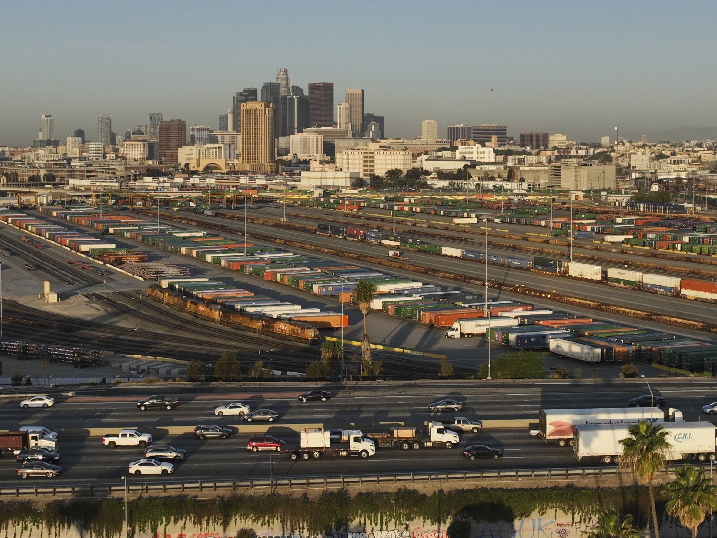 caption: Traffic flows on Interstate 5 past shipping containers near downtown Los Angeles, Tuesday, April 8, 2025.