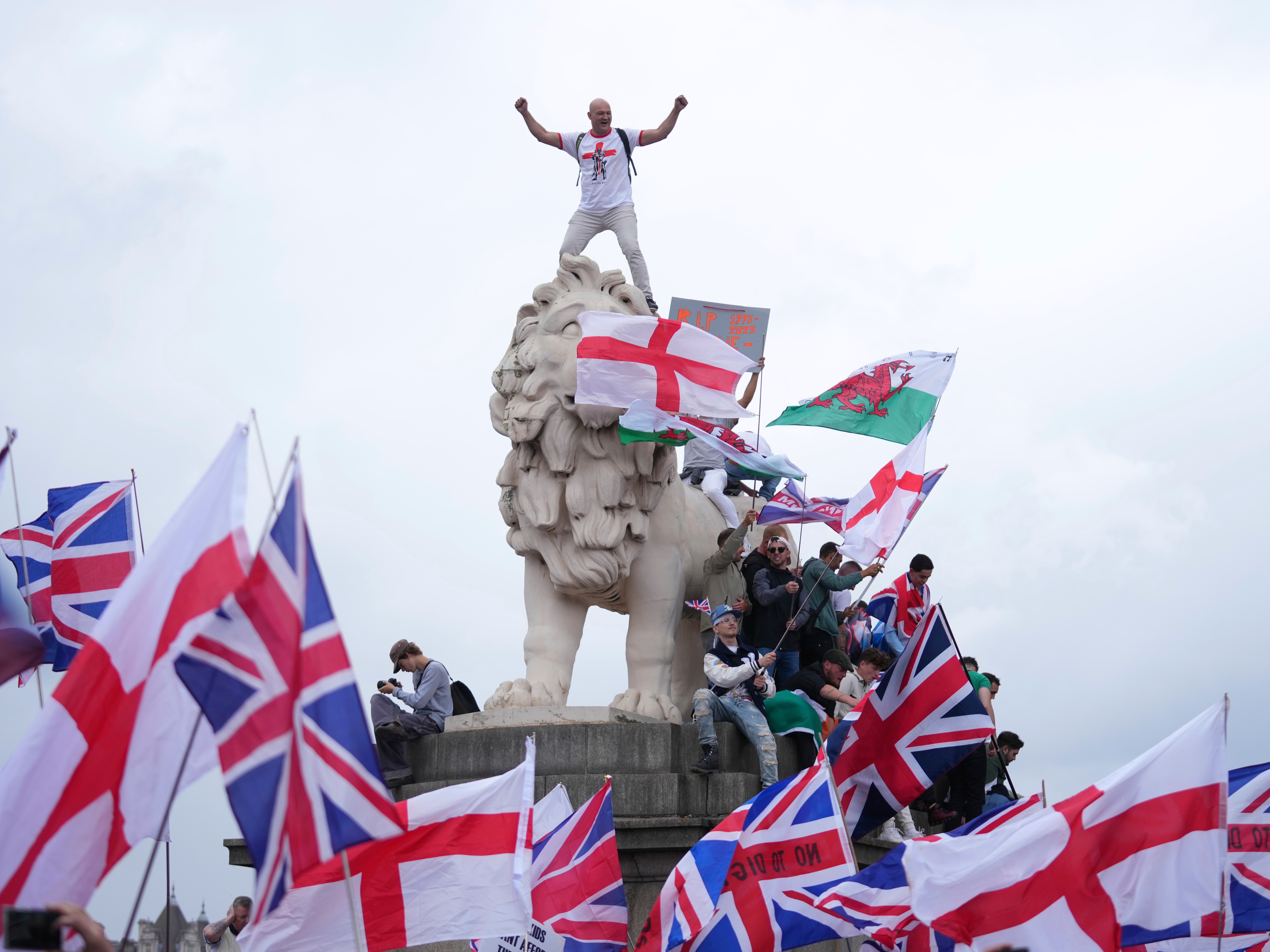 caption: A demonstrator stands on the head of the South Bank lion that sits on the side of the Westminster Bridge, during a Tommy Robinson-led Unite the Kingdom march and rally in London, on Saturday.