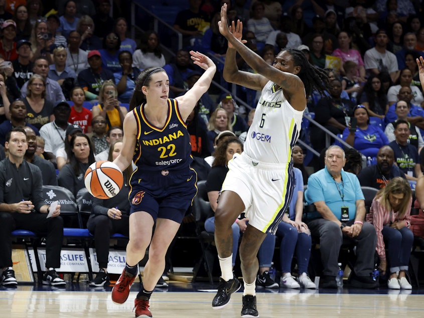 caption: Indiana Fever guard Caitlin Clark (22) drives past Dallas Wings forward Natasha Howard (6) during their WNBA basketball game in Arlington, Texas, on Friday.