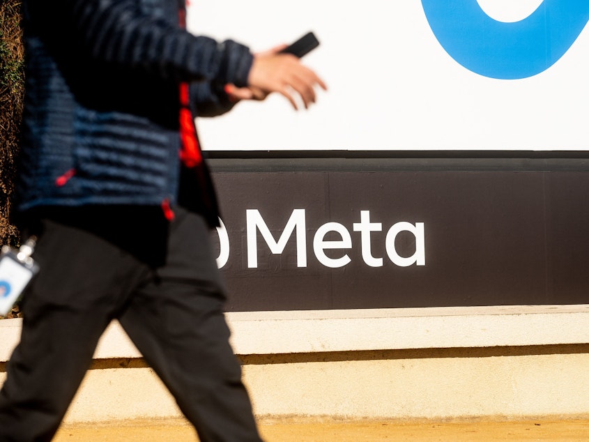 caption: A person walks past a sign bearing Meta's logo at the company's Menlo Park headquarters in October 2021. The company is introducing new safety measures for younger Instagram users after facing widespread scrutiny.