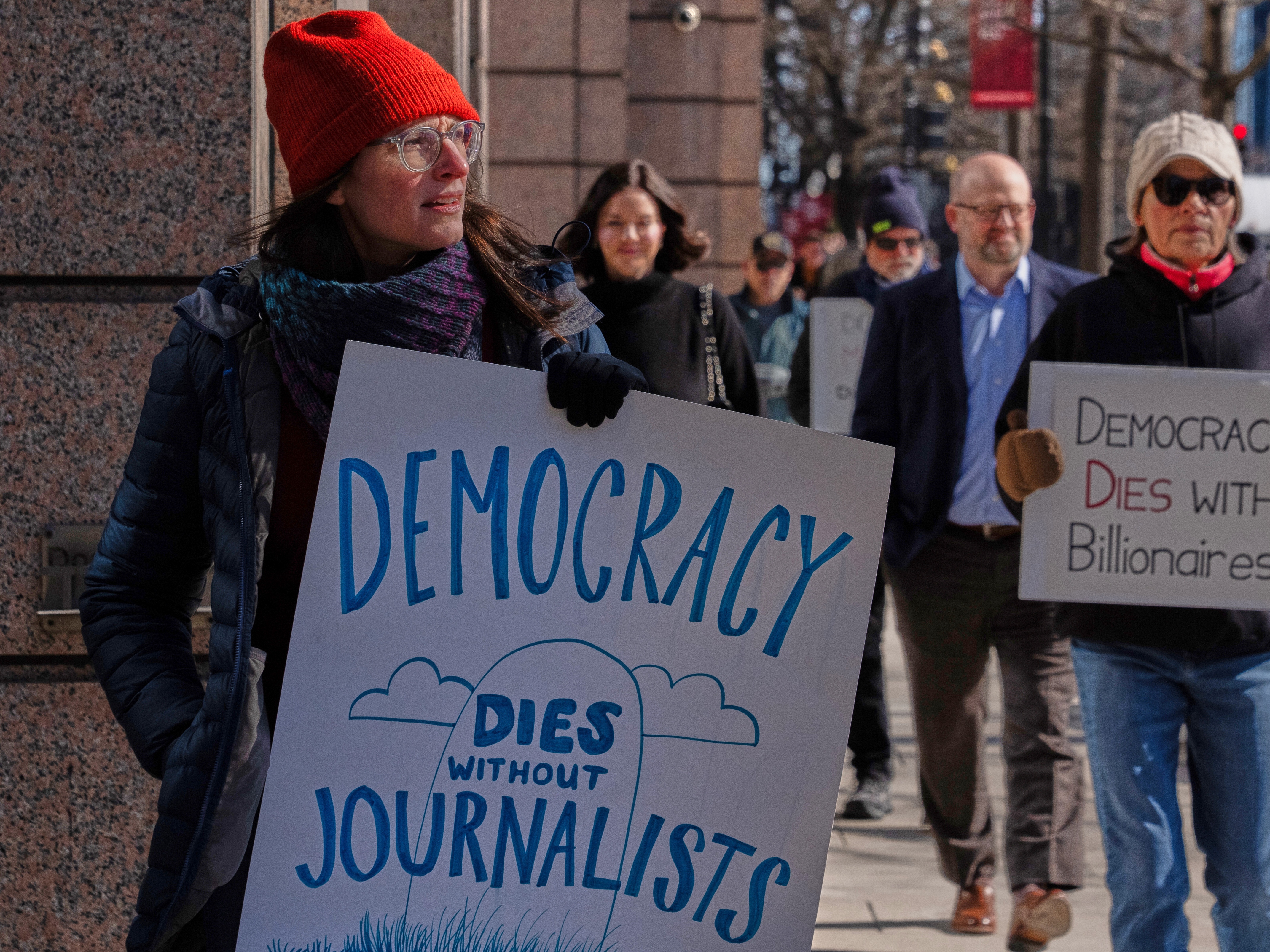caption: Sarah Kaplan, a Washington Post journalist, protests outside of the newspaper's headquarters on Thursday, Feb. 5, 2026. That same day, CEO Will Lewis was photographed at the NFL Honors in San Francisco.