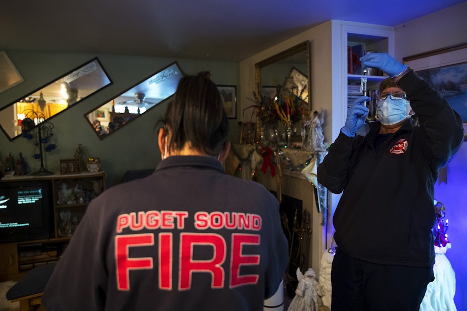 caption: Puget Sound Regional Firefighters Jessi Nemens, left, and Nikki Smith, right, get ready to administer a Moderna Covid-19 vaccine for Jonell, a homebound individual who preferred to give her first name only, at her home on Monday, May 24, 2021, in Kent.