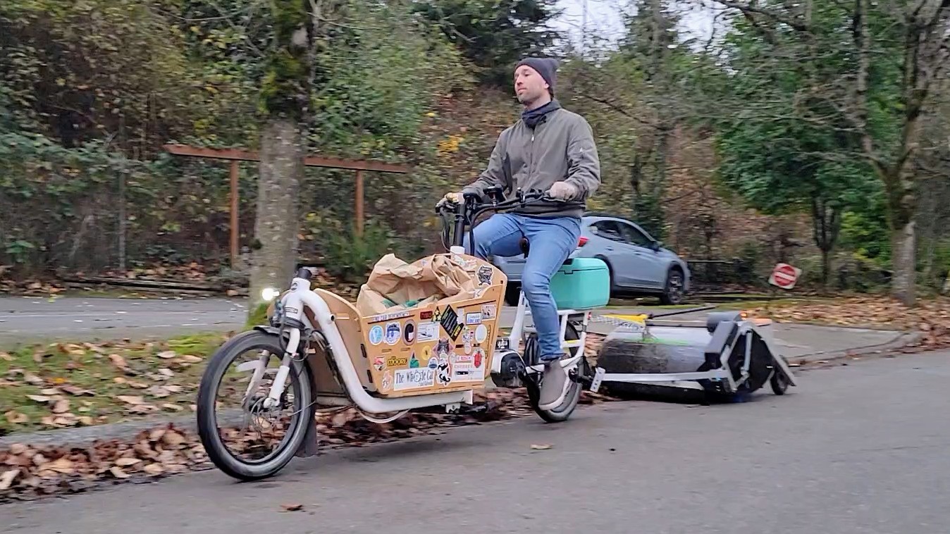 caption: Charlie Liban pulls a bike-lane sweeper behind his e-bike in Kirkland on Friday, Nov. 21, 2025.
