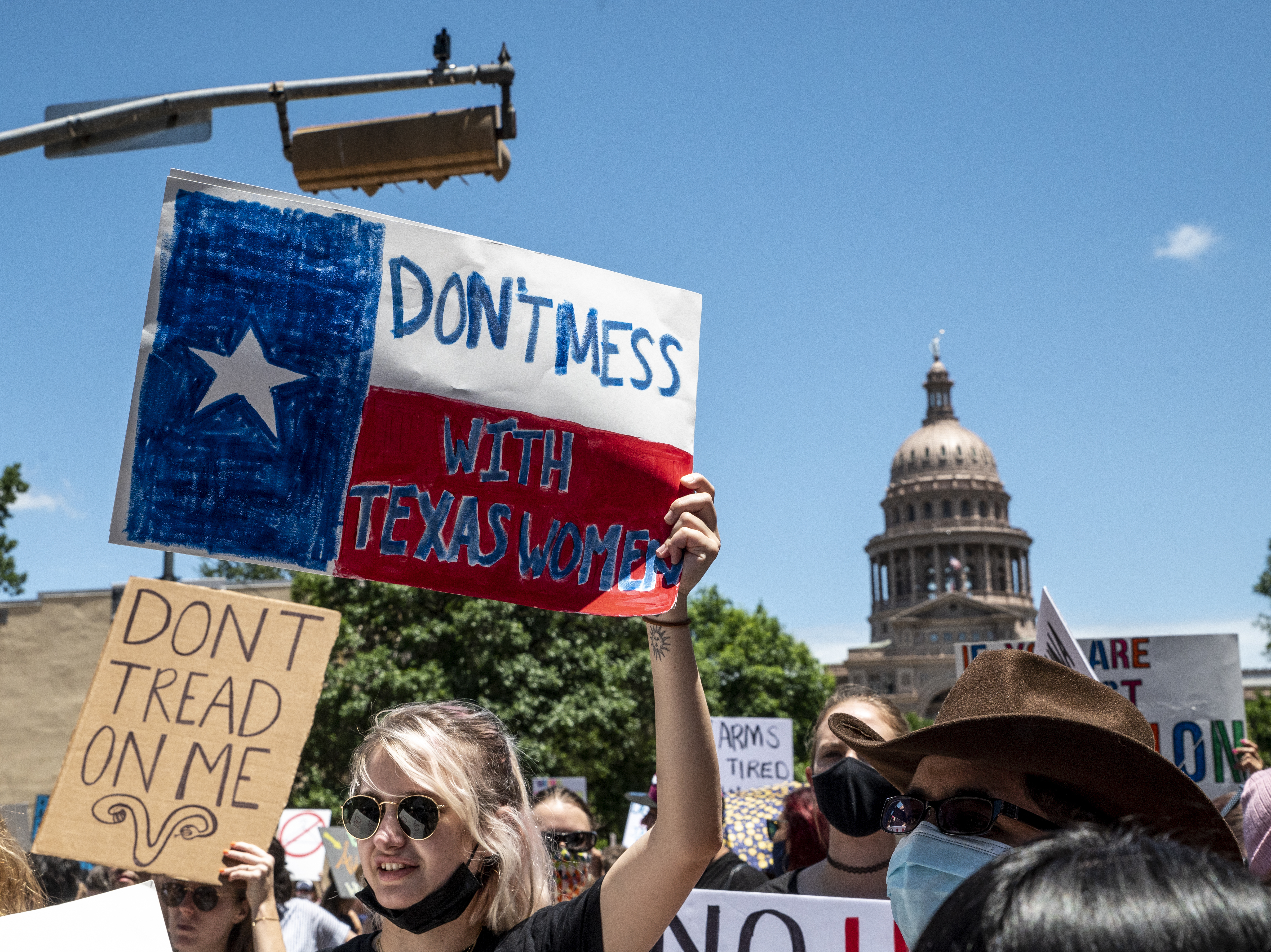 caption: Protesters hold signs as they march in opposition to the anti-abortion law S.B. 8 outside the Texas state capitol on May 29, 2021 in Austin.