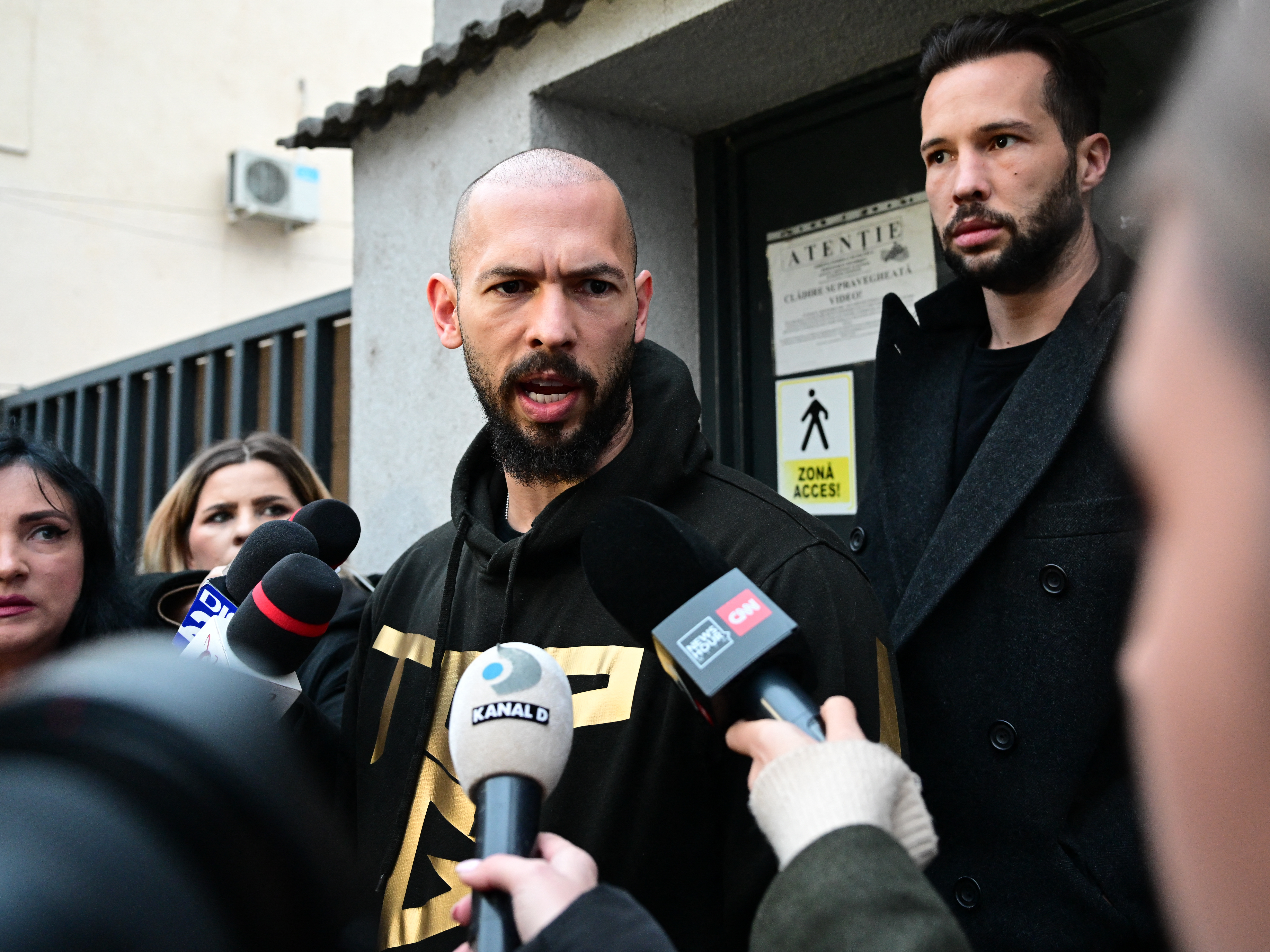 caption: British U.S. former professional kickboxer and controversial influencer Andrew Tate (center) and his brother Tristan Tate (back right) speak to journalists after having been released from detention in Bucharest, Romania, Tuesday.