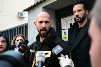 caption: British U.S. former professional kickboxer and controversial influencer Andrew Tate (center) and his brother Tristan Tate (back right) speak to journalists after having been released from detention in Bucharest, Romania, Tuesday.