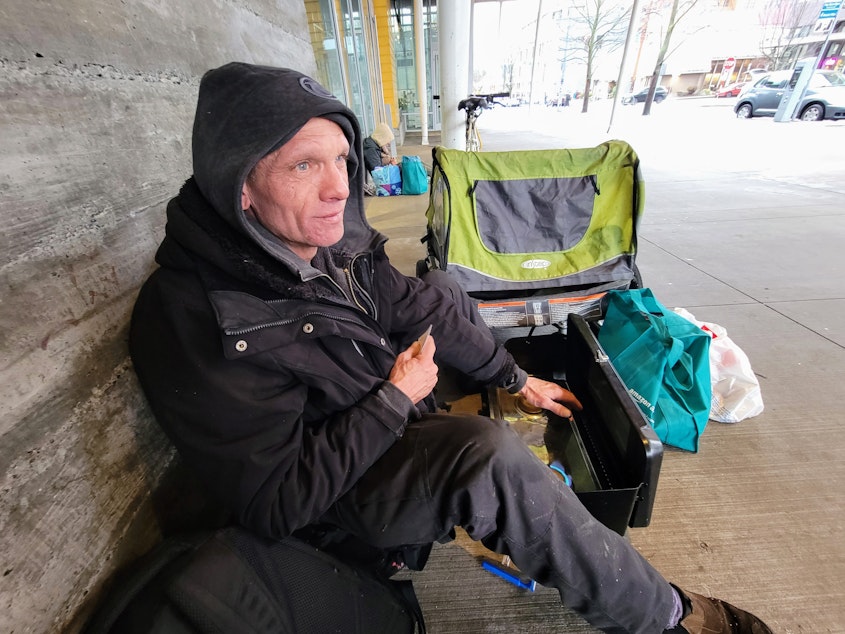 caption: Howard Cartwright sits outside the Seattle Library Ballard branch on Wednesday, Jan. 17, 2024.