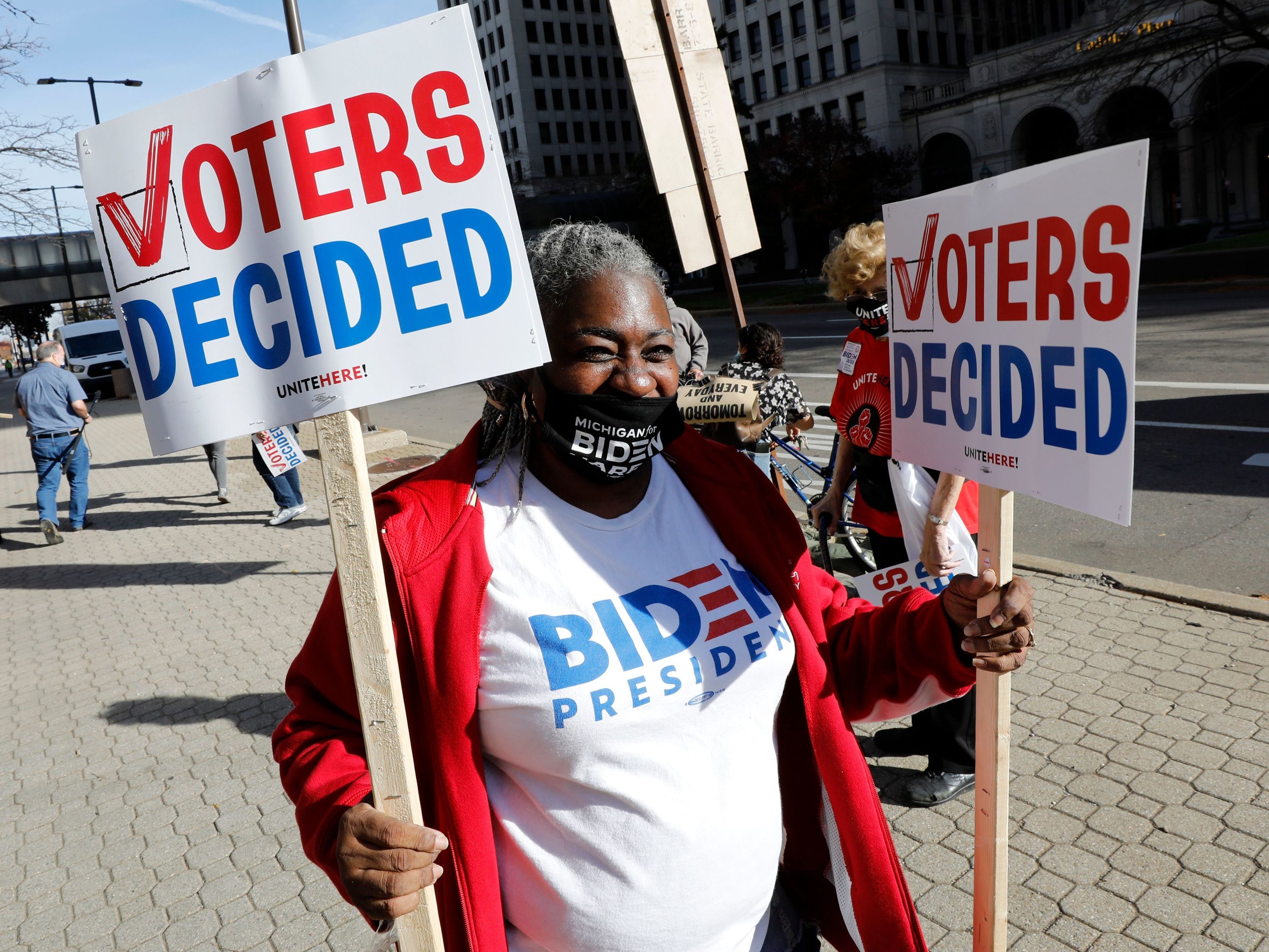 caption: Zinnia Patcas hands out signs in Detroit on Nov. 7 as people gather to celebrate Joe Biden's win in the presidential election.