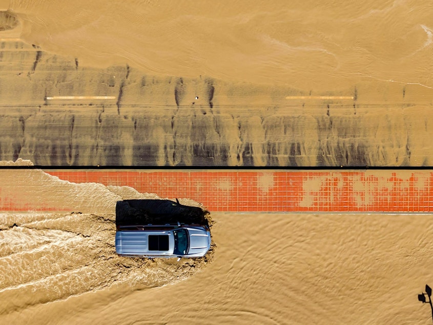 caption: In this aerial picture taken on Aug. 21, a vehicle drives through floodwaters following heavy rains from Tropical Storm Hilary in Thousand Palms, Calif.