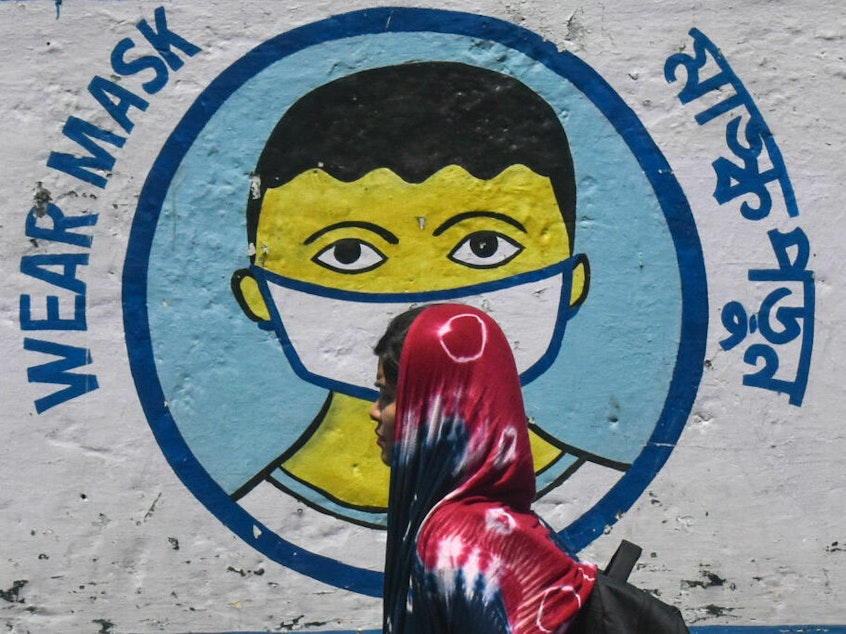 caption: A poster in Kolkata, India, from peak pandemic days sends a message to mask up. Now that the official COVID-19 global emergency is no longer in effect, some folks are thrilled to stop masking — but others wonder if it's a good idea to keep up certain precautions.