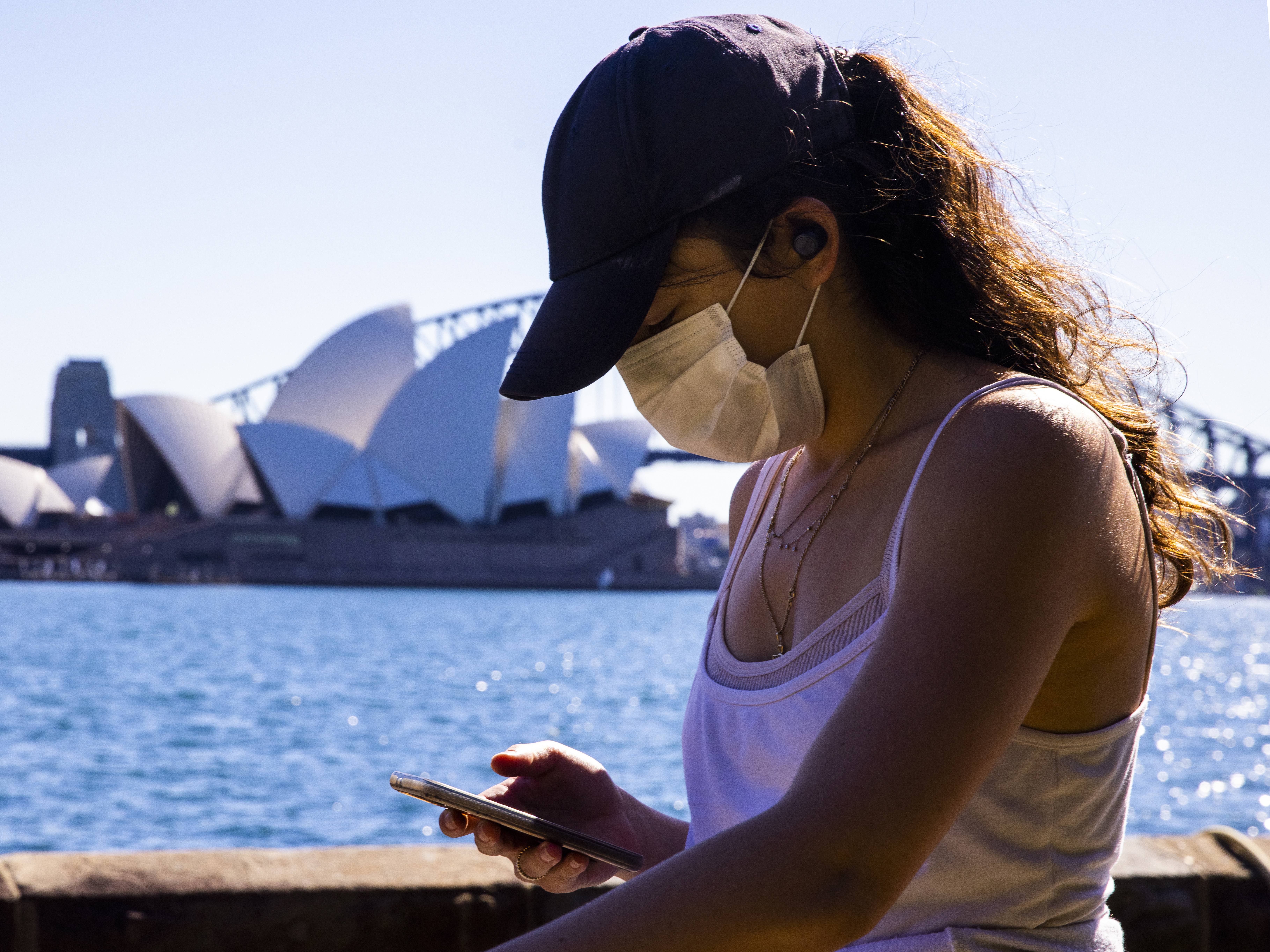 caption: A woman looks at her phone outside the The Royal Botanic Gardens in Sydney, Australia on Aug. 6. The Indicator from Planet Money spoke to an economist for advice on how to cut back on digital dependency.