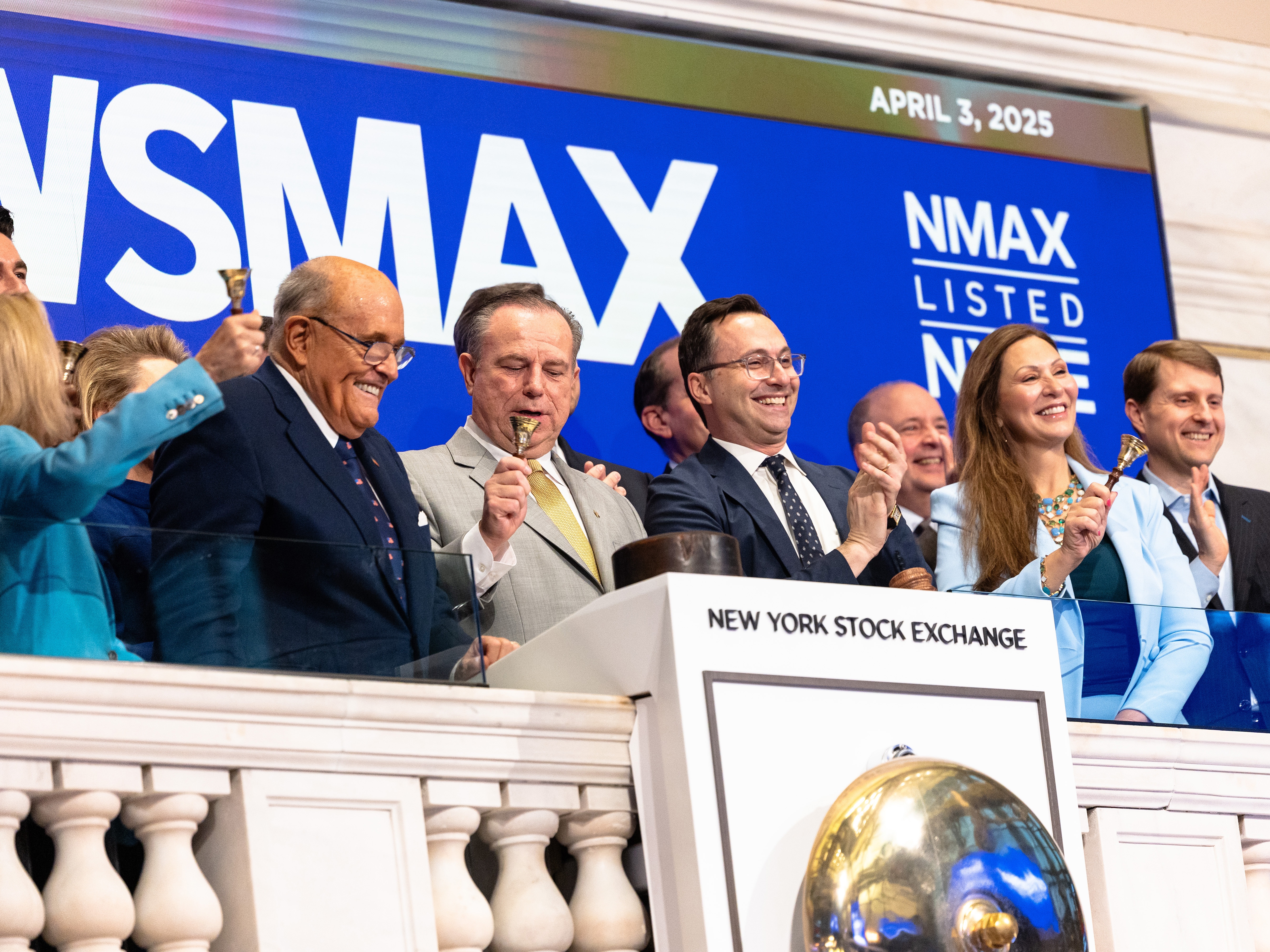 caption: Newsmax will pay $67 million to Dominion Voting Systems to settle a lawsuit over the network's coverage of the 2020 presidential election. In this photo from April 3, 2025, Newsmax CEO Chris Ruddy and former New York City Mayor Rudy Giuliani join others at the opening of trading at the New York Stock Exchange.