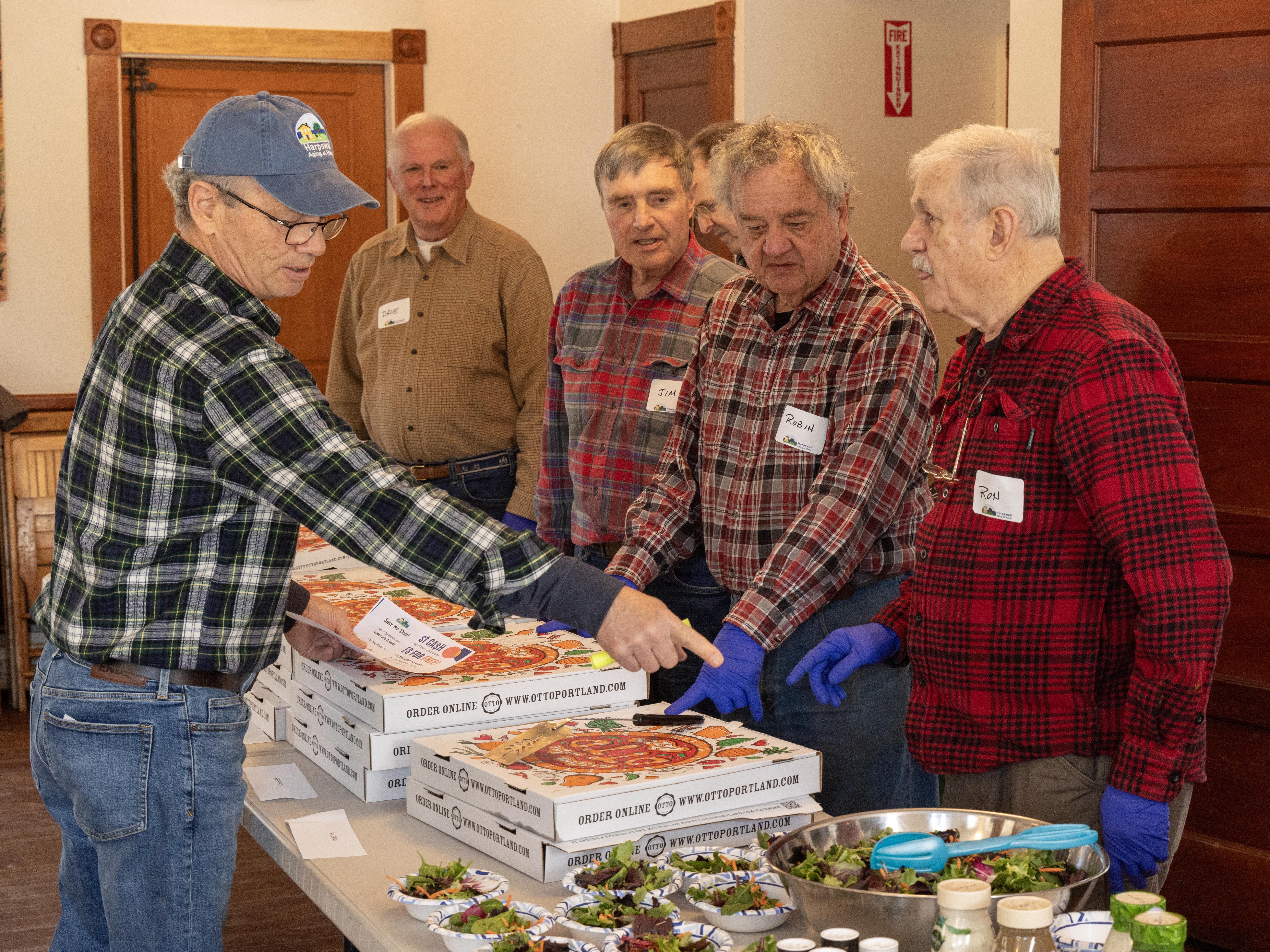 caption: Attendance has more than quadrupled since the free ROMEO lunches for older men started in Harpswell, Maine, last fall. Tom Mahoney, left, directs other volunteers at a recent lunch when pizza was on the menu.
