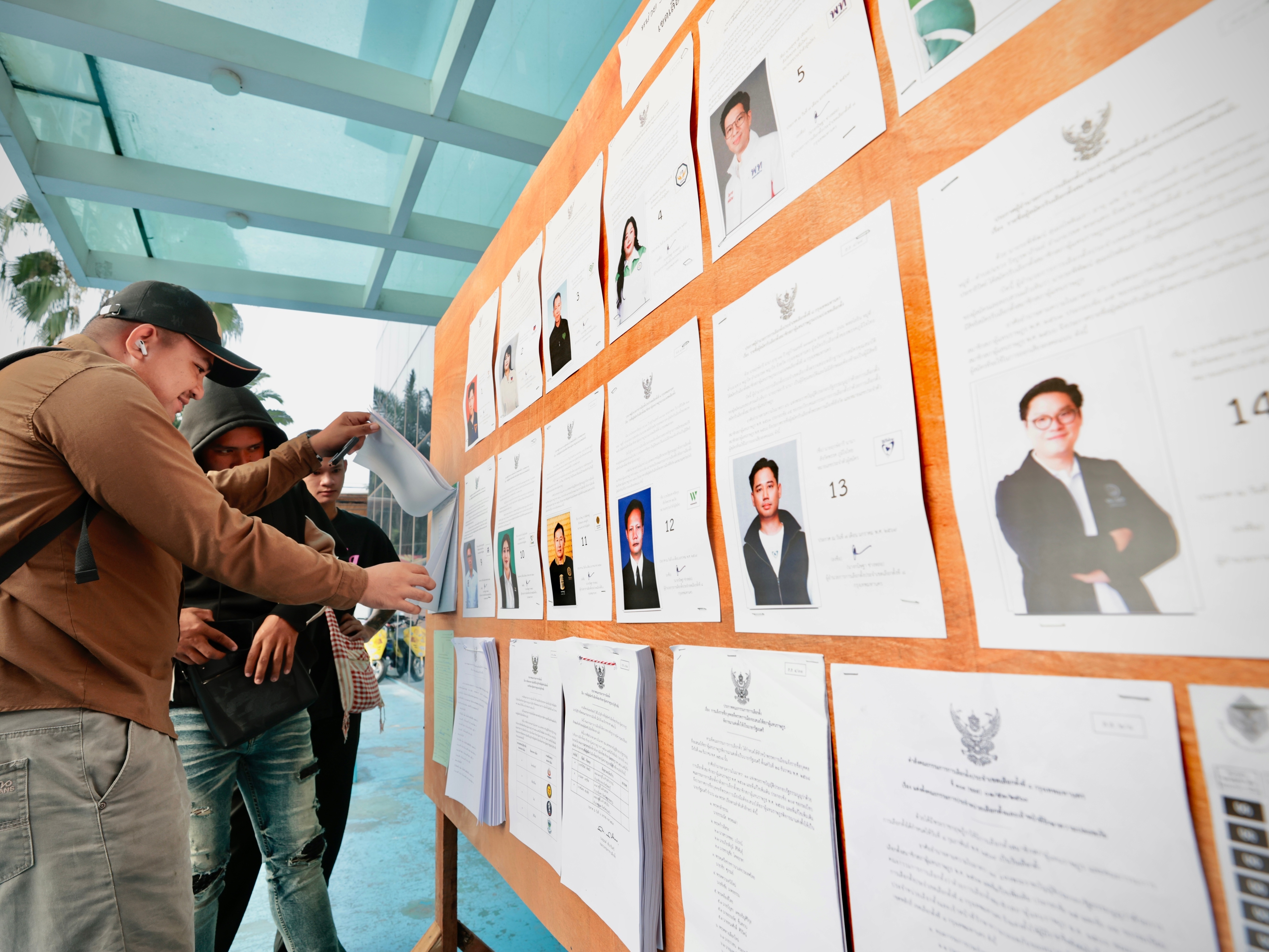 caption: Voters look at candidates listed on a display board before entering a voting station for the general election in Bangkok, on Sunday, Feb. 8, 2026.