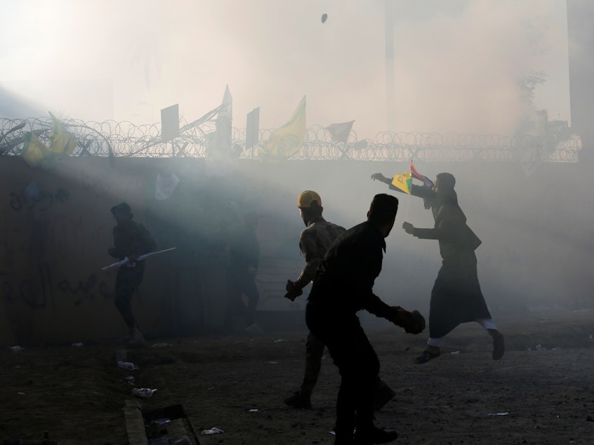 caption: Protesters and militia members throw stones toward the U.S. Embassy in Baghdad on Tuesday.