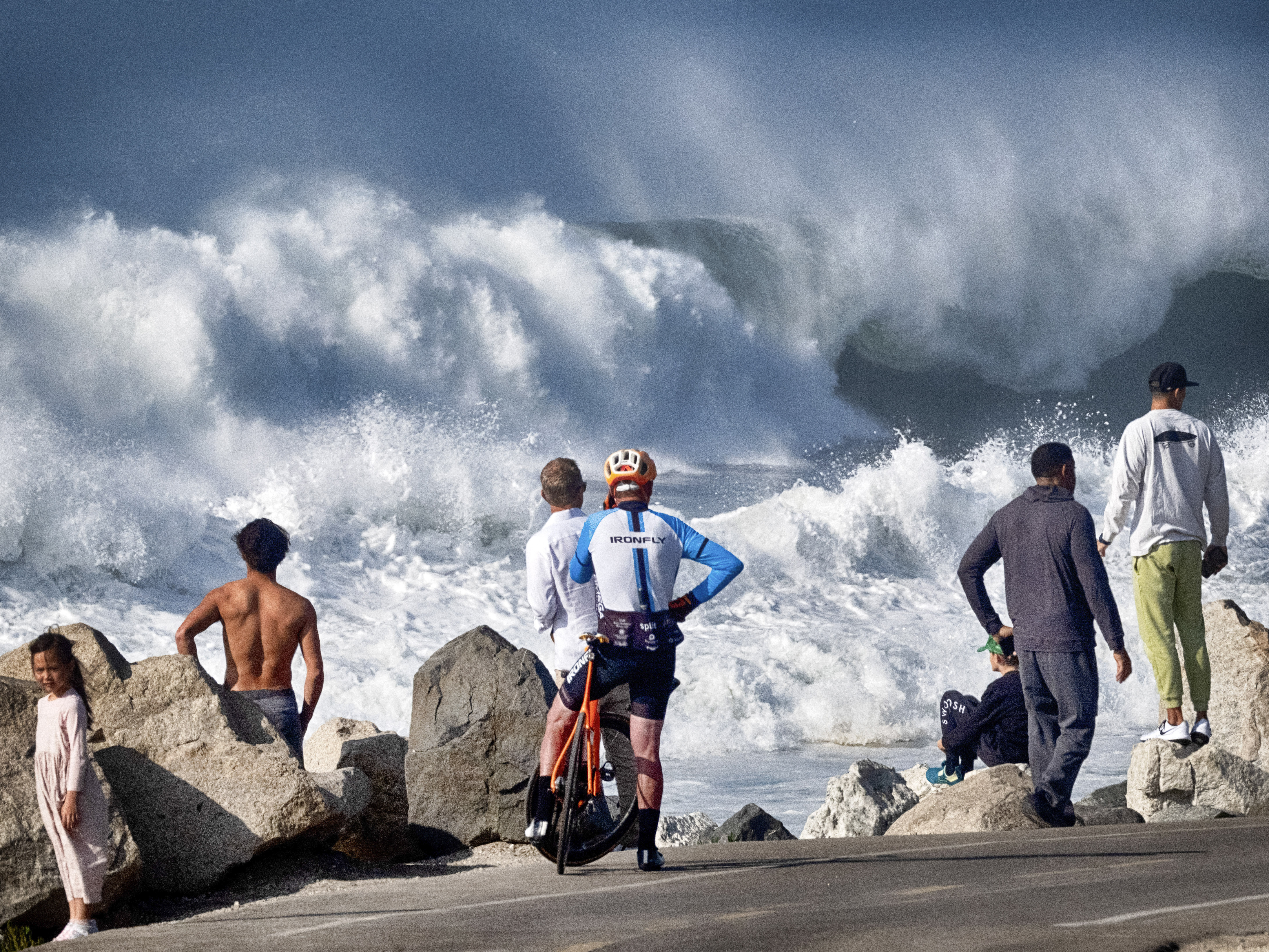 caption: Beachgoers watch as turbulent surf pounds the coast on Thursday in Manhattan Beach, Calif.