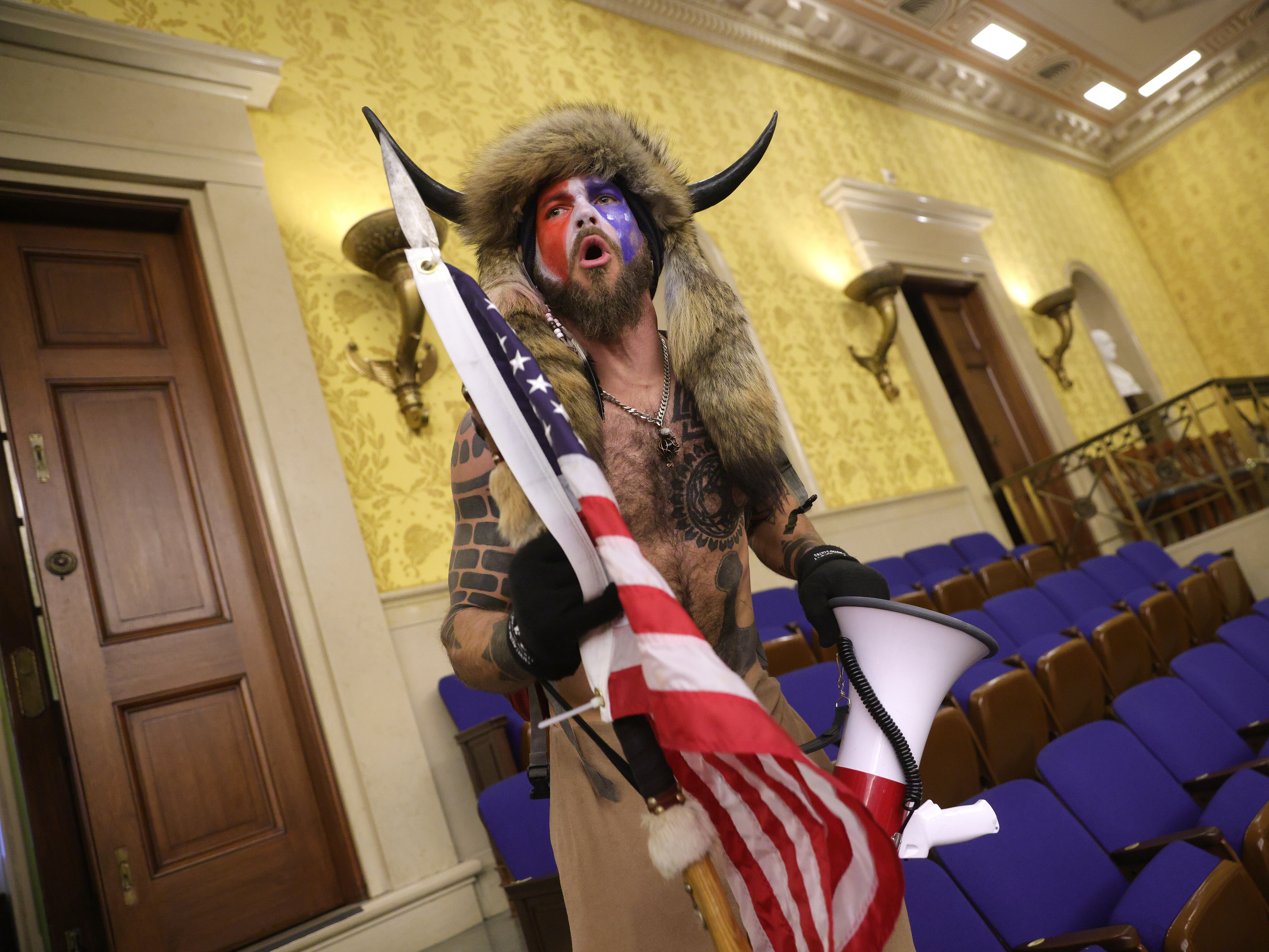 caption: Jacob Chansley, photographed during the Jan. 6 U.S. Capitol insurrection, screams "Freedom" inside the Senate chamber following the breach of a mob during a joint session of Congress.