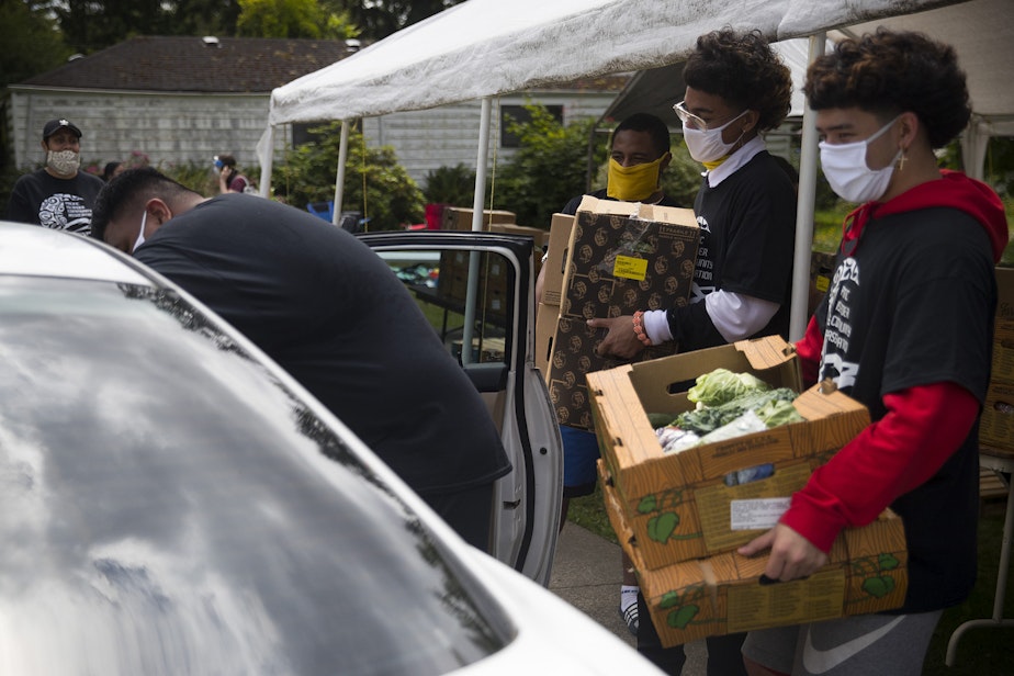 caption: Koa Derouin, right, loads boxes of fresh produce, meat and dairy into vehicles at a drive-thru free food distribution site led by the Pacific Islander Community Association of Washington on Thursday, July 10, 2020, along Military Road South in Kent. 