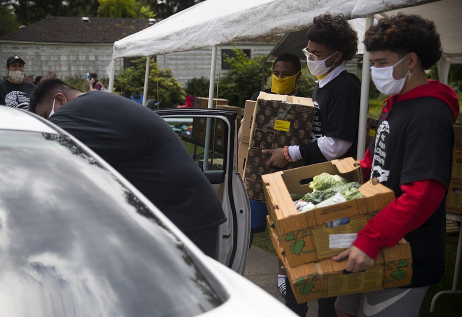 caption: Koa Derouin, right, loads boxes of fresh produce, meat and dairy into vehicles at a drive-thru free food distribution site led by the Pacific Islander Community Association of Washington on Thursday, July 10, 2020, along Military Road South in Kent. 