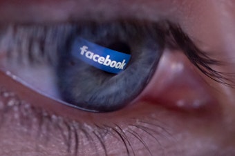 caption: The social platform Facebook logo reflects in the pupil of an eye.