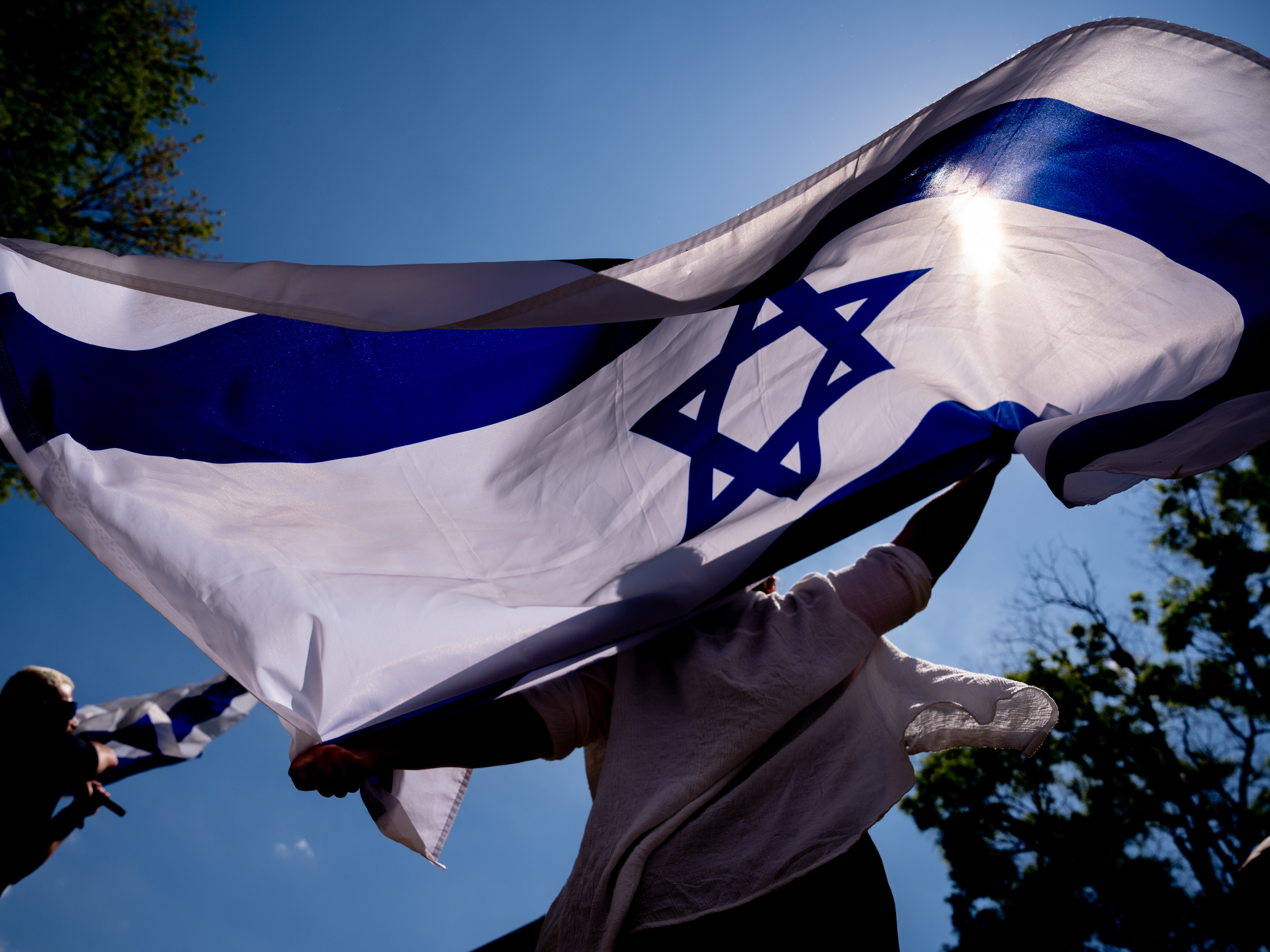 caption: People dance and wave large Israeli flags during a rally against campus antisemitism at George Washington University in May 2024 in Washington, D.C.