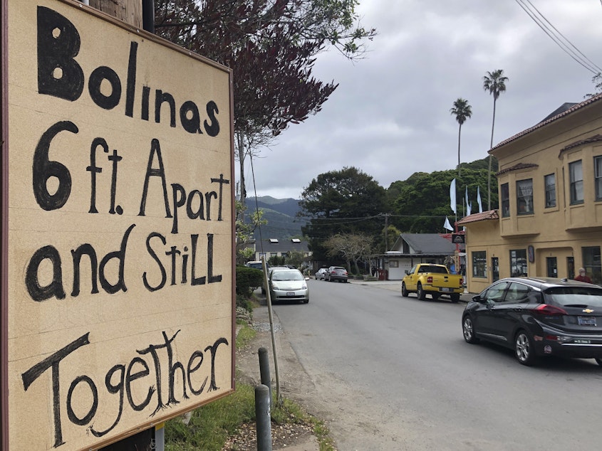 caption: A sign about being 6 feet apart is posted along the main road through Bolinas, Calif. Residents are undergoing testing as part of a coronavirus study.