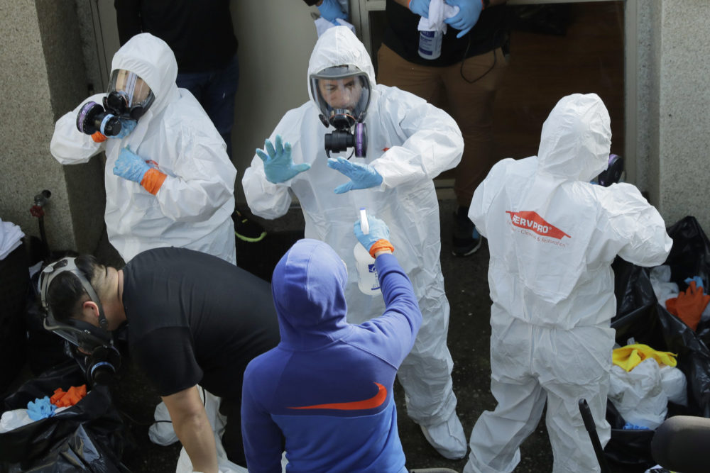 caption: Servpro cleaning workers are sprayed as they exit the Life Care Center in Kirkland, Wash., Thursday, March 12, 2020, at the end of a day spent cleaning inside the facility near Seattle. (Ted S. Warren/AP Photo)