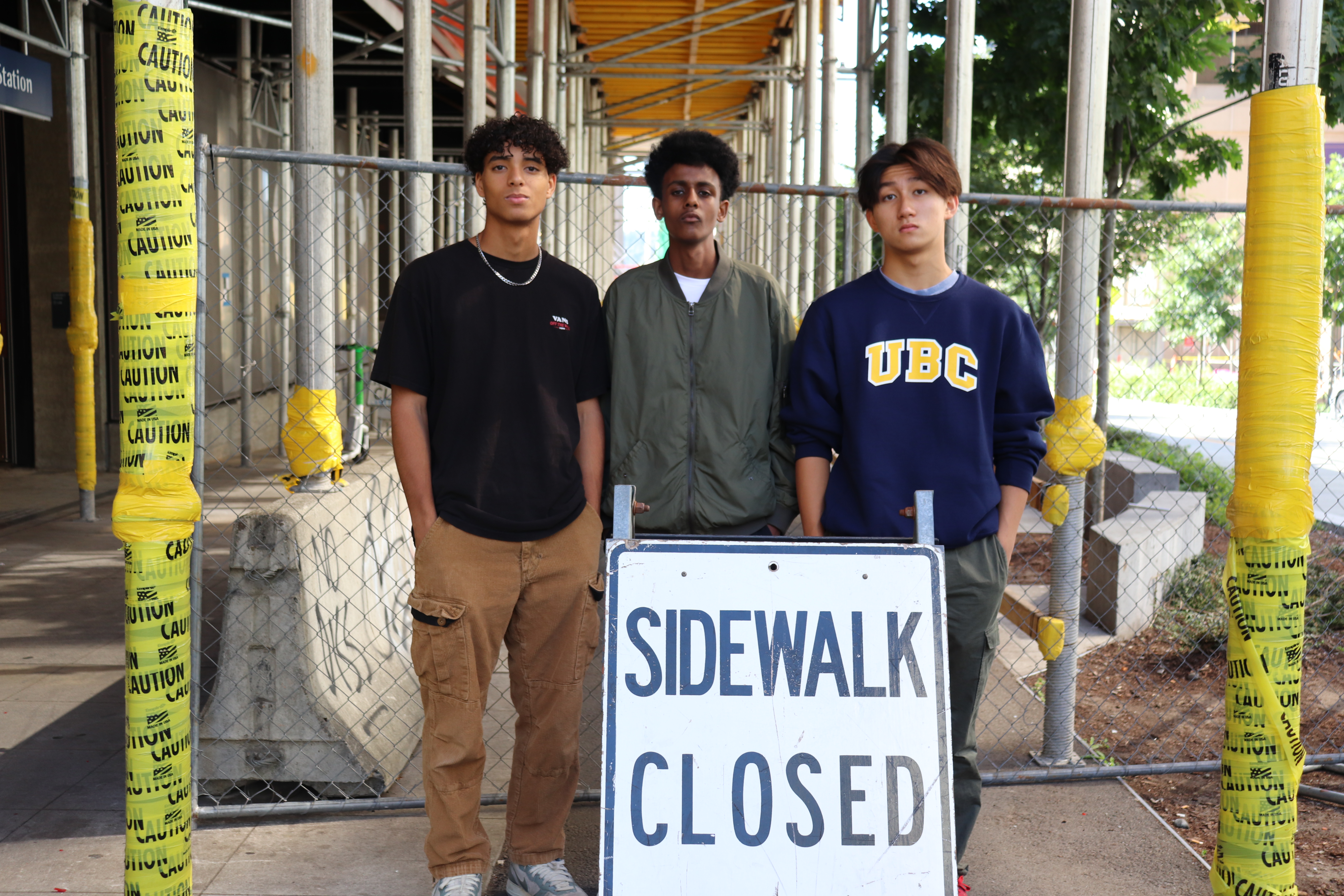 caption: Gavin Muhlfelder (left), Alex Mengisteab and Phillip Zhou pose in front of the University District Link light rail station in July 2023.