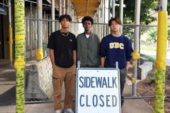 caption: Gavin Muhlfelder (left), Alex Mengisteab and Phillip Zhou pose in front of the University District Link light rail station in July 2023.