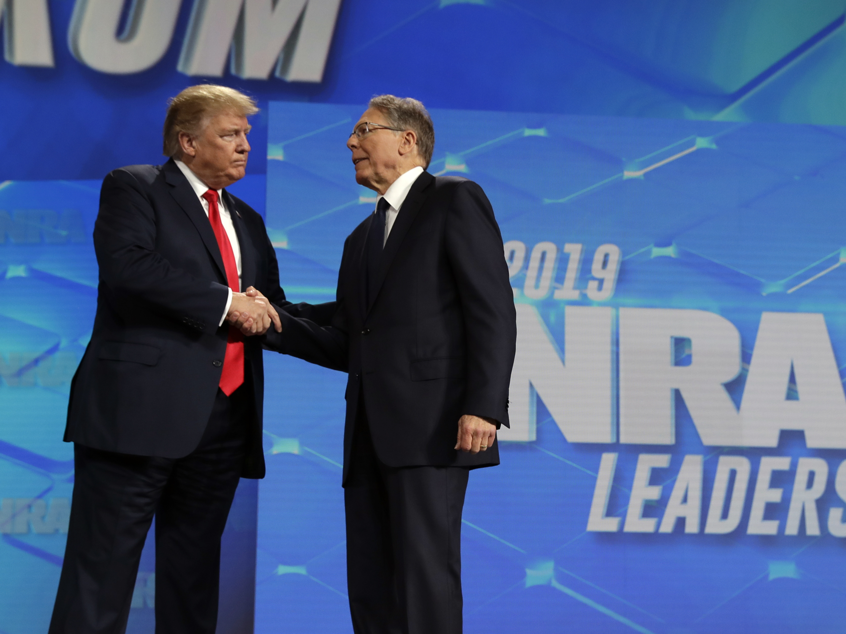 caption: President Donald Trump shakes hands with NRA Executive Vice president and CEO Wayne LaPierre, at the annual meeting of the National Rifle Association on April 26, 2019, in Indianapolis. The NRA is going ahead with its annual meeting in Houston just days after the shooting massacre at a Texas elementary school.