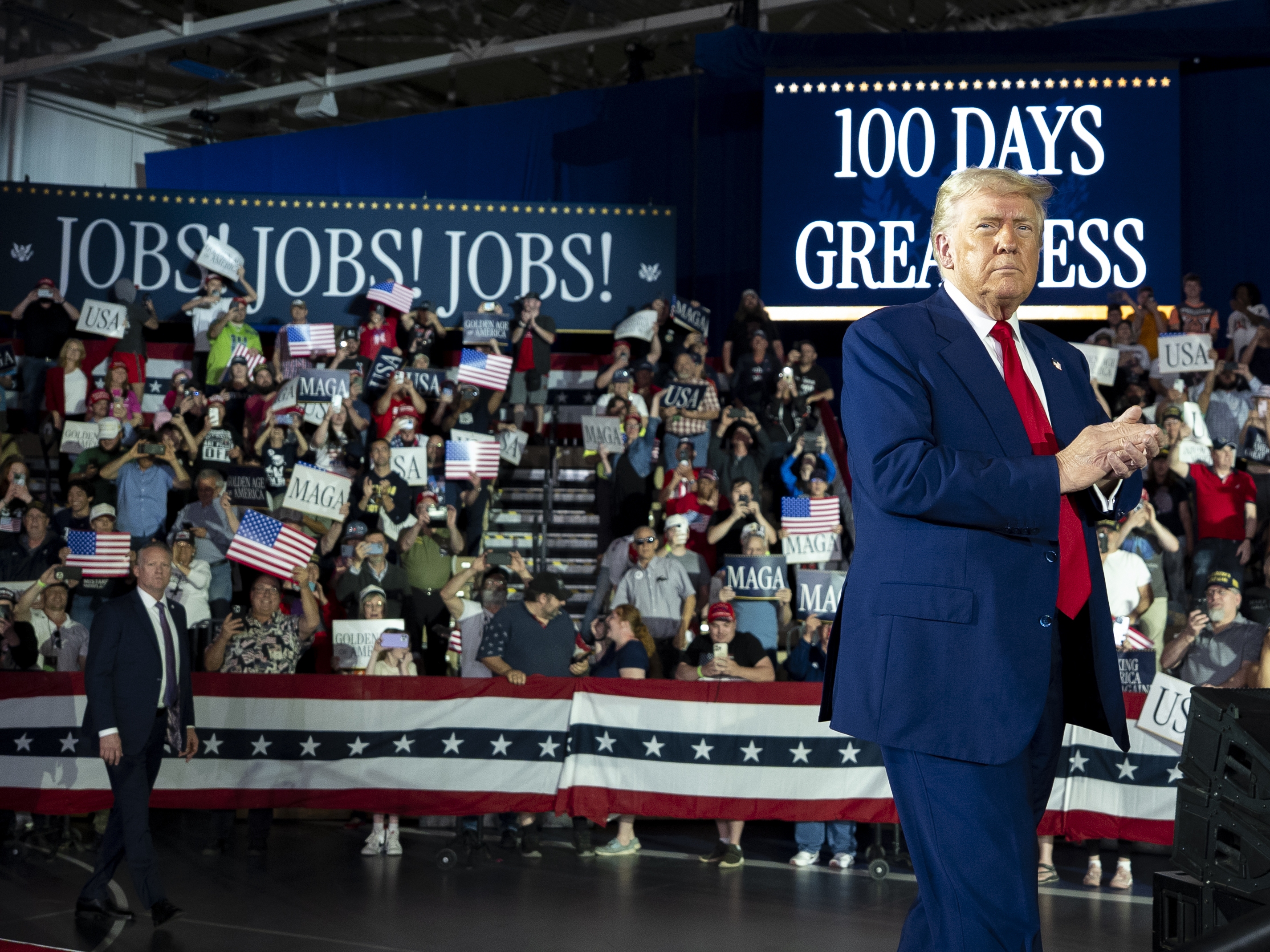 caption: President Trump arrives to speak on his first 100 days at Macomb County Community College Sports Expo Center on April 29 in Warren, Mich.
