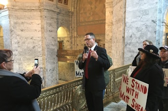 caption: Republican state Rep. Matt Shea records a video on the first day of the legislative session while a small group of supporters gather around him.