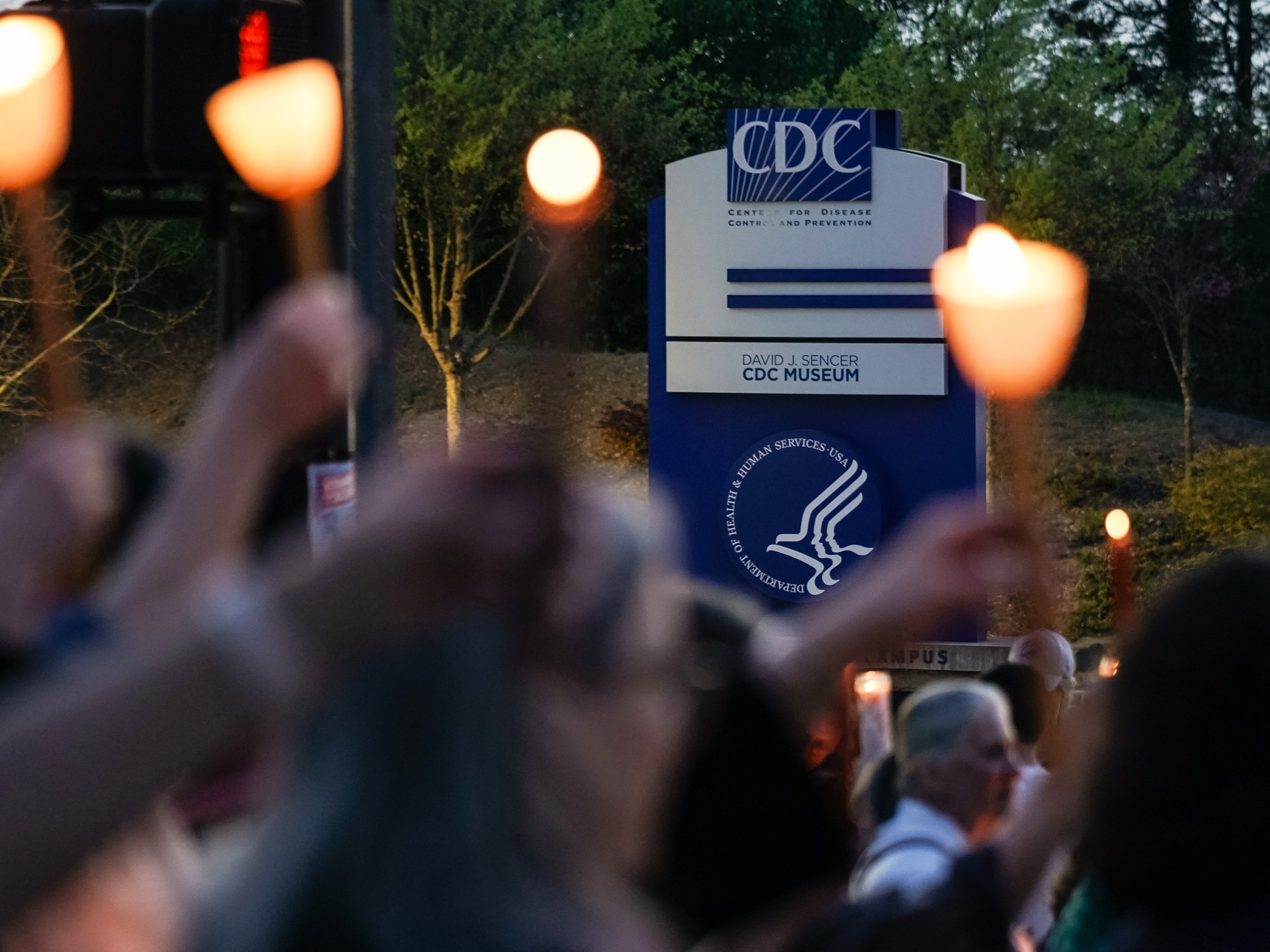 caption: People participate in a candlelight vigil in front of the main offices of the Centers for Disease Control in Atlanta on March 28, days before thousands of CDC employees were laid off.