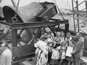 caption: A group of former displaced persons helps to load the Freedom Bell aboard a Navy transport vessel in Brooklyn, New York, Oct. 9, 1950. One of the children, Eva Zandler, 8, originally from Poland, presents a scroll to be enshrined in the Freedom Bell Tower in Berlin, to Frederick Osborn, New York City chairman for the Crusade for Freedom.