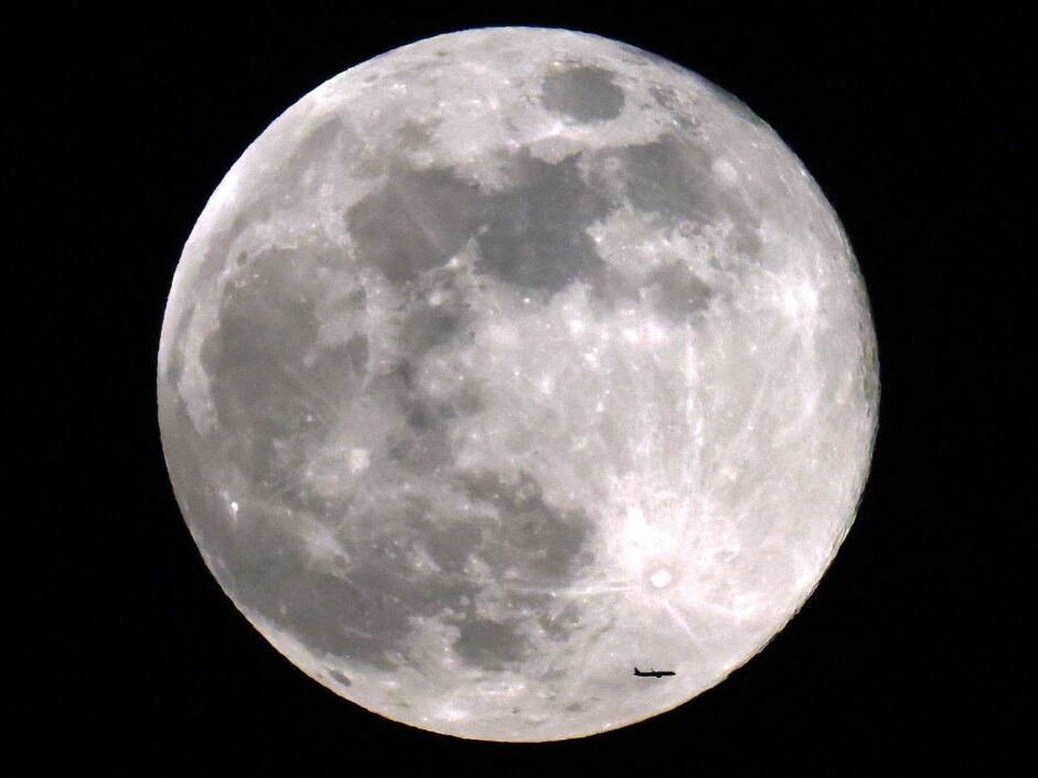 caption: A commercial airliner flies before the rising Beaver full moon above Kuwait City on Nov. 27, 2023.