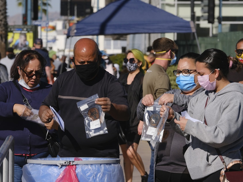 caption: People drop their test kits into a receptacle at a coronavirus testing site in the North Hollywood section of Los Angeles on Saturday. With COVID-19 cases surging at a record pace in California, Gov. Gavin Newsom has warned that the state's hospitals could soon be overwhelmed.