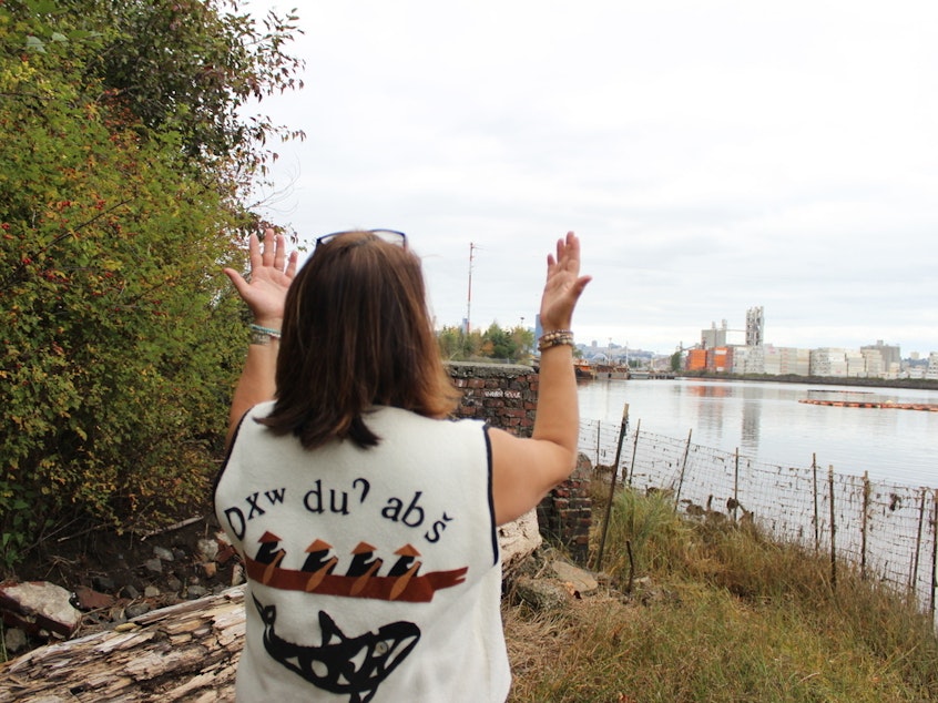 caption: Duwamish Tribal Services Executive Director Jolene Haas holds up her hands, a traditional gesture of gratitude, on the banks of the Duwamish River in Seattle on Sept. 21, 2019.