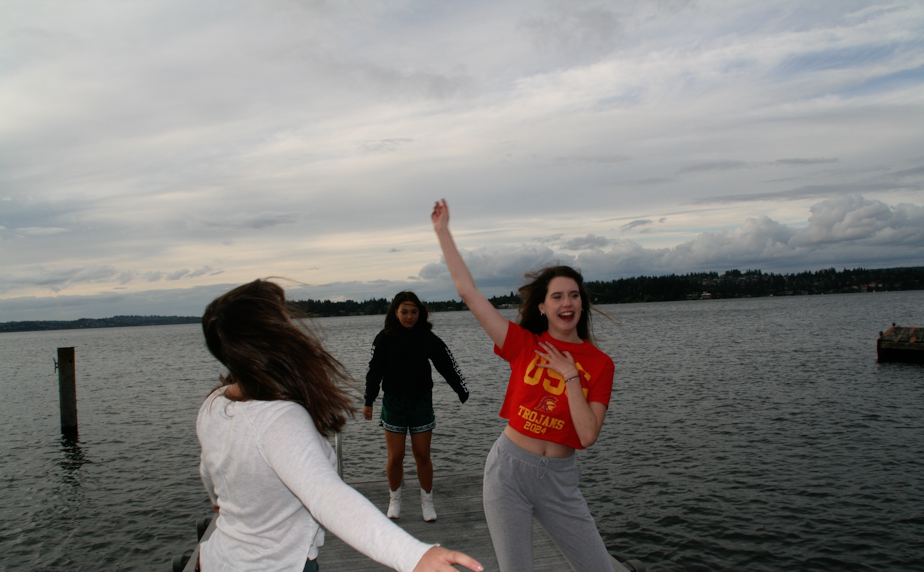 caption: Mercer Island High School graduating seniors (from left to right) Isabel Funk, Annie Poole, and Elizabeth Gottesman dance to music on a Mercer Island dock on June 8, 2020, the evening before graduation. Instead of a senior graduation party, attended by many, these seniors spent the time together as a smaller group. 