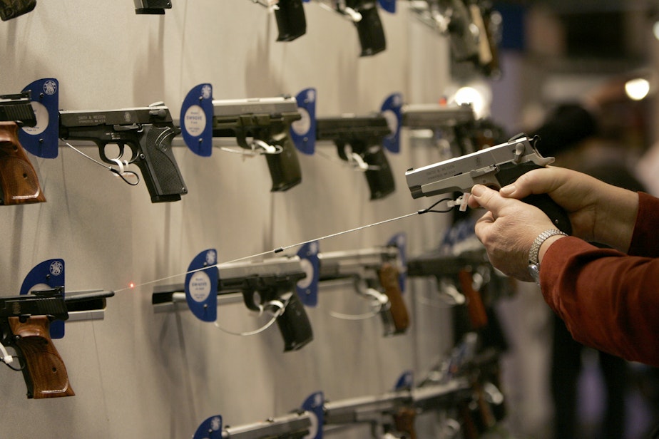 caption: A woman points a handgun with a laser sight on a wall display of other guns during the National Rifle Association convention Friday, April 13, 2007, in St. Louis. 