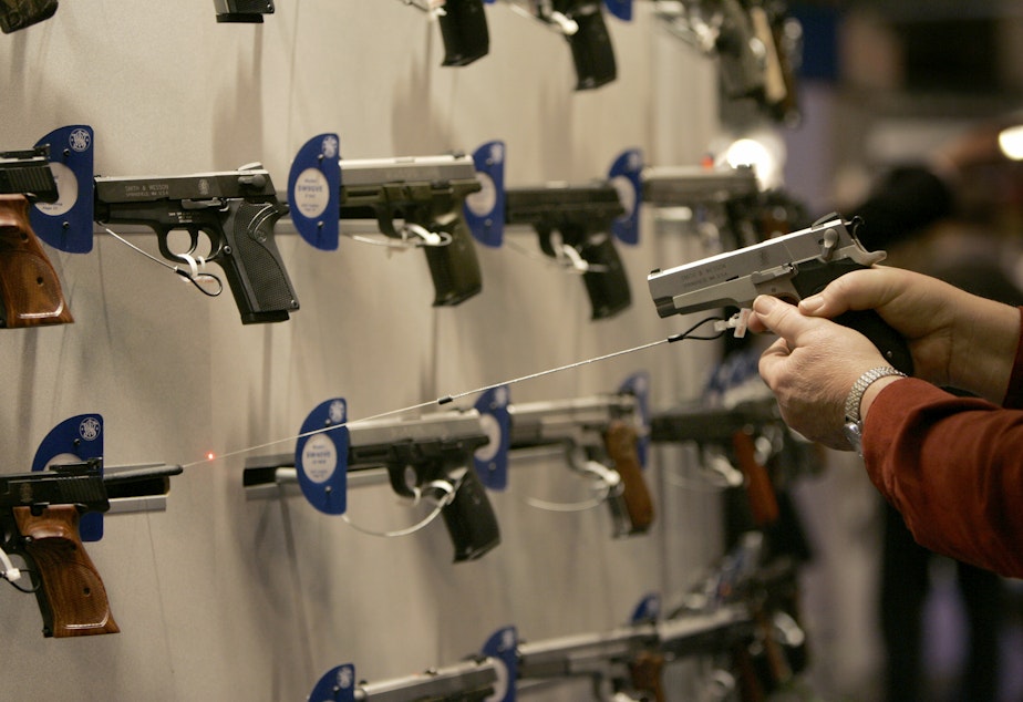 caption: A woman points a handgun with a laser sight on a wall display of other guns during the National Rifle Association convention Friday, April 13, 2007, in St. Louis. 