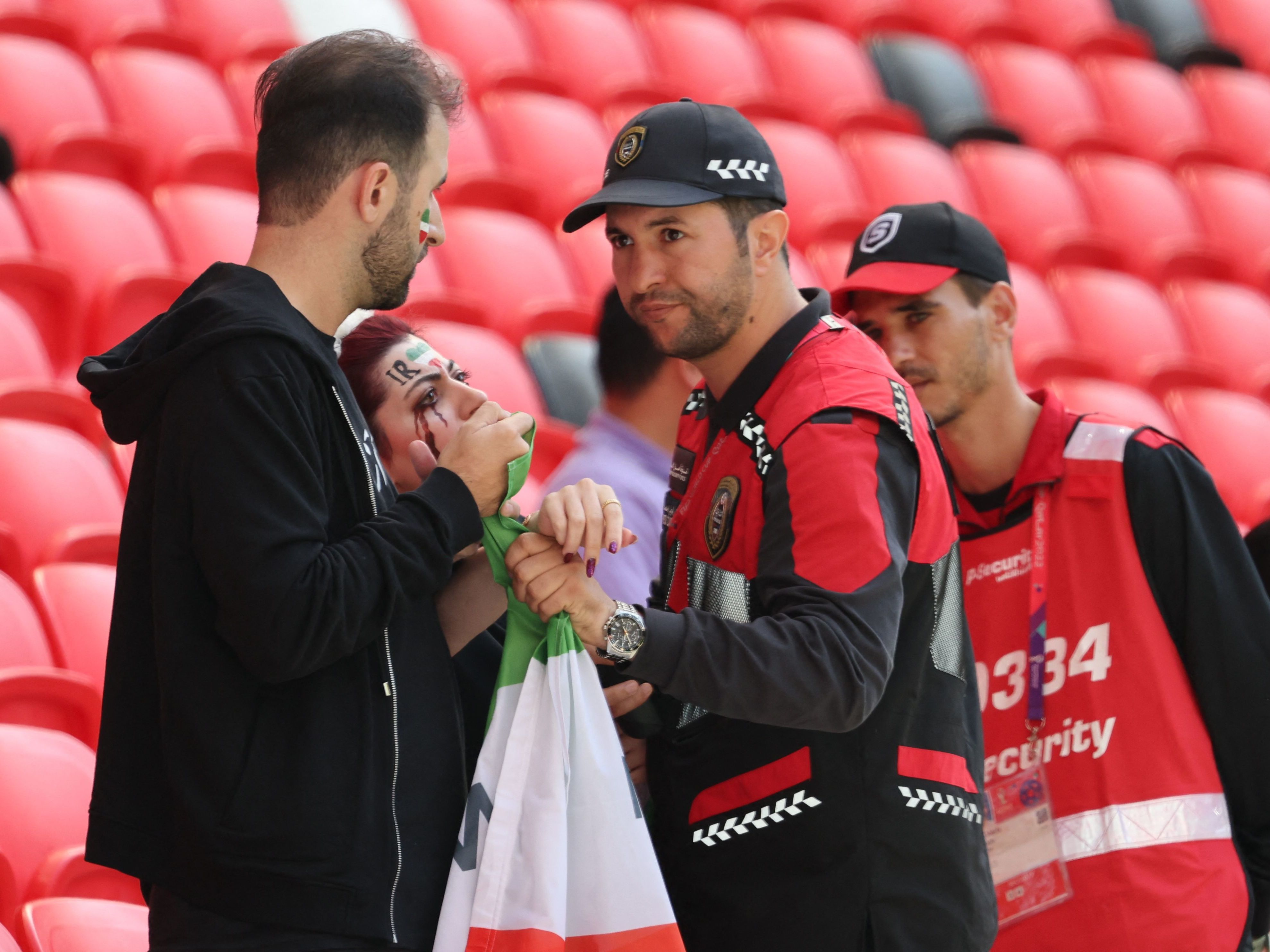 caption: Members of security, right, speak with two Iran supporters as they take away a flag reading "Woman life freedom" prior to the match between Wales and Iran on Nov. 25.
