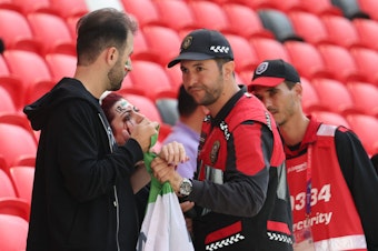 caption: Members of security, right, speak with two Iran supporters as they take away a flag reading "Woman life freedom" prior to the match between Wales and Iran on Nov. 25.