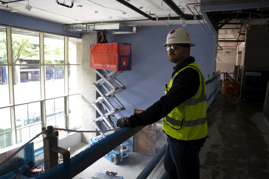 caption: Garrett Metz, senior project engineer at Skanska, looks on as construction continues at the site of a new apartment building on Monday, June 17, 2024, along Third Avenue in Seattle.