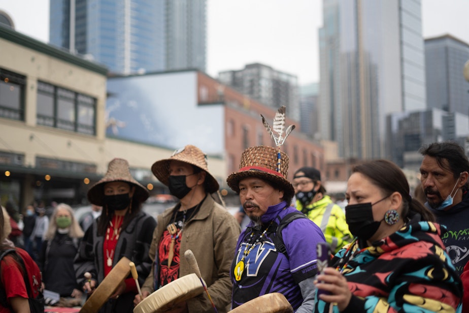 caption: Swinomish tribal senator Eric (Stooltsa) Day, center, joins other drummers in song near the 24-foot totem pole carved by the House of Tears Carvers of the Lummi Nation, on Saturday, May 22, 2021, outside of Seattle’s Pike Place Market. 