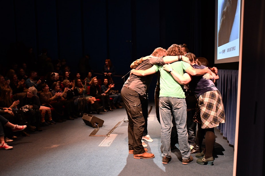 caption: All the performers hug as the audience applaud at KUOW's Stories from THE WILD event on Friday, October 11, 2019, at McCaw Hall in Seattle.

