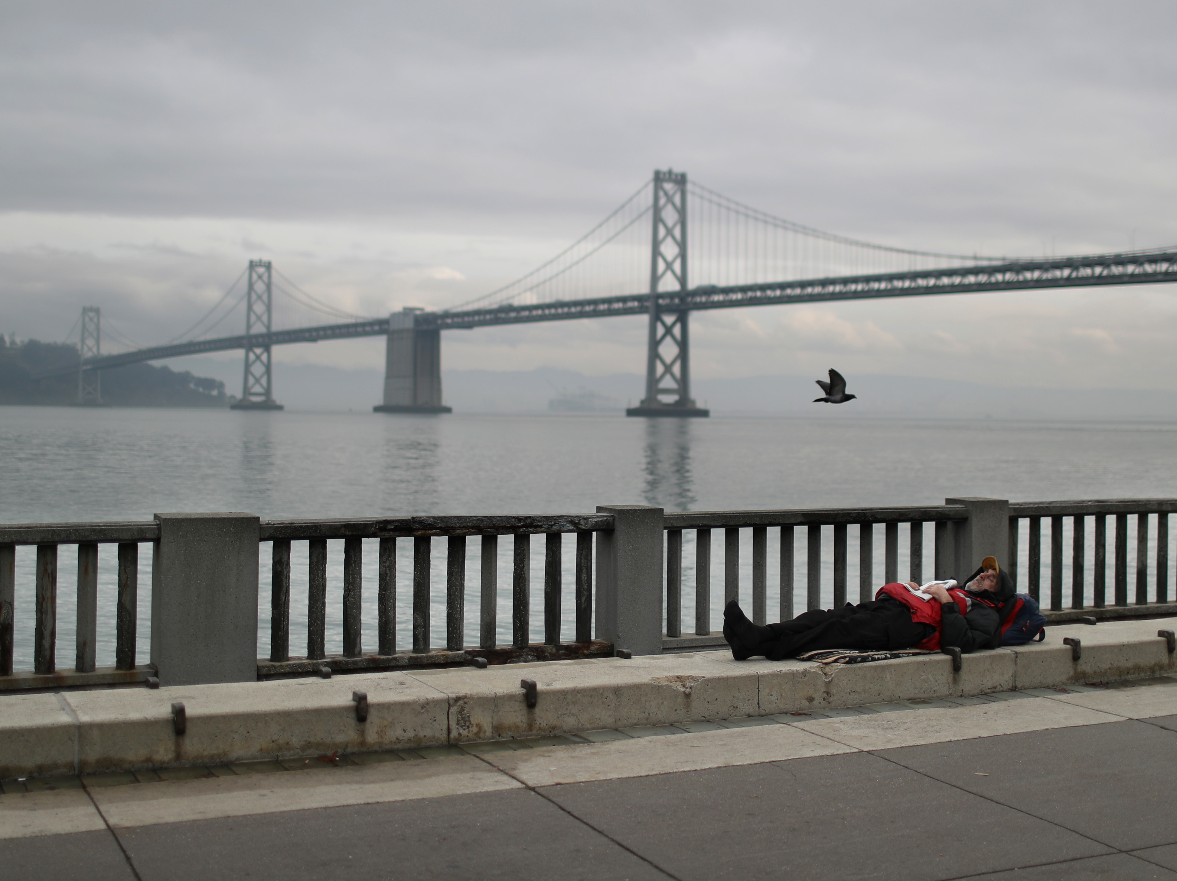 SAN FRANCISCO, CALIFORNIA - DECEMBER 05: A homeless man sleeps on the sidewalk near the San Francisco–Oakland Bay Bridge on December 05, 2019 in San Francisco, California.
