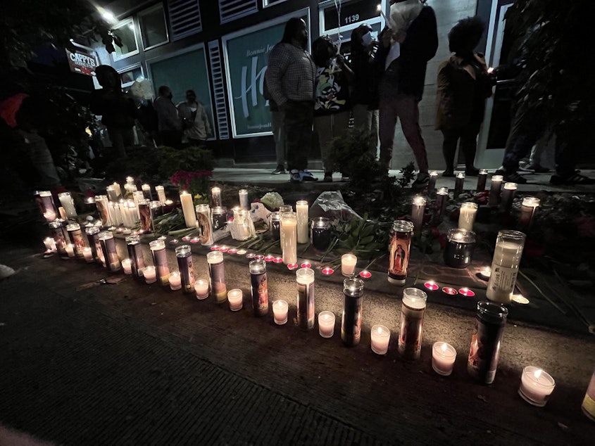 caption: Candles light the sidewalk near The Postman in Seattle's Central District in remembrance of D'Vonne Pickett Jr. Thursday, Oct. 20, 2022. Pickett died a day earlier at a bus stop near his shop on Martin Luther King Jr. Way.